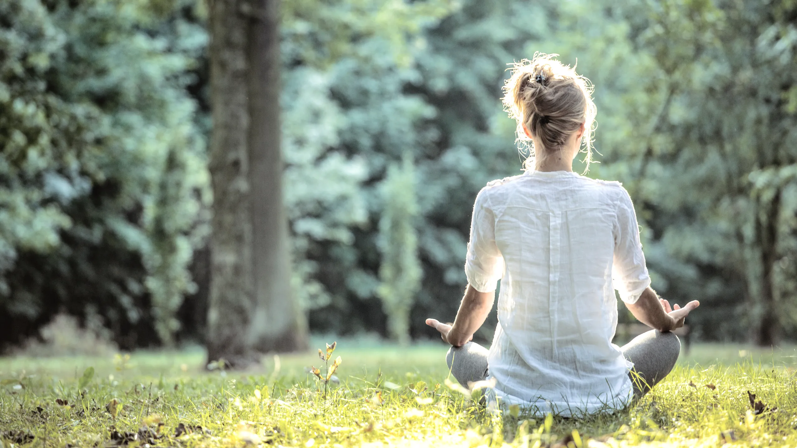 Frau sitzt meditierend im Gras in der Natur und praktiziert Achtsamkeit für Körper und Geist